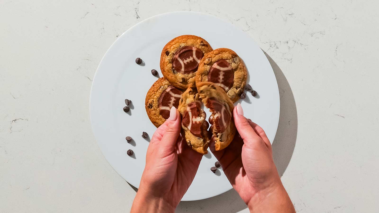 Person breaking open a double stack cookie with football shapes on top.