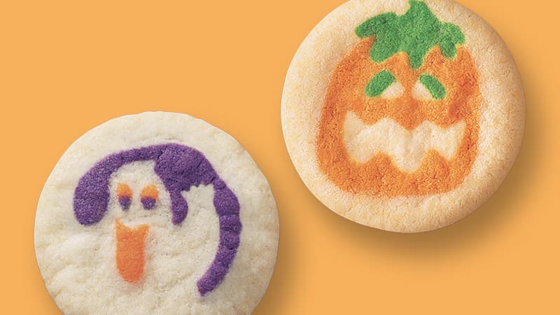 Two Halloween cookies: one with a pumpkin face and the other with a ghost face, both on an orange background.
