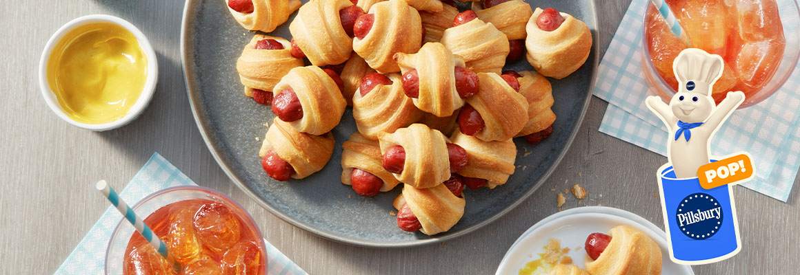 A plate of pigs in a blanket with bowls of various dips. 
