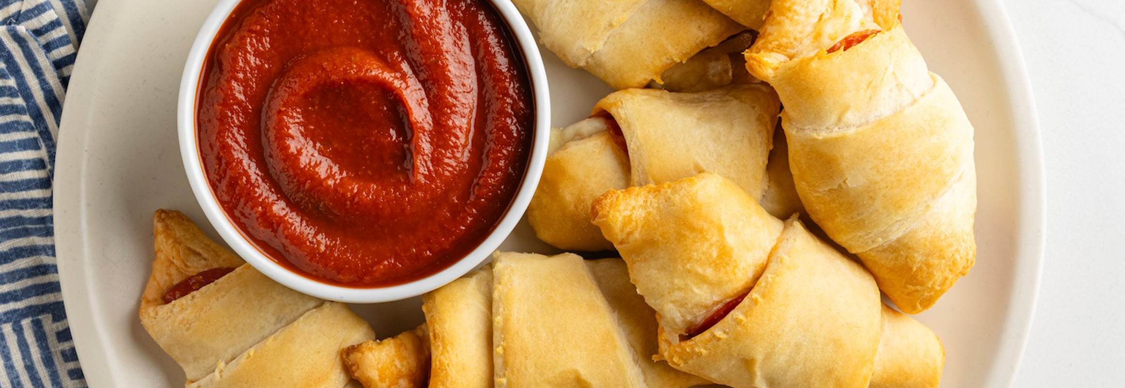 Cheese and pepperoni crescent rolls on a white plate served with marinara dipping sauce.